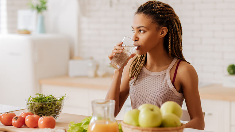 decorative image of woman drinking water with fruit on the table