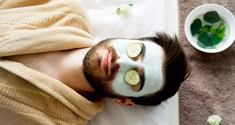 Decorative image showing a man using a clay face mask with cucumber on his eyes to show the benefits